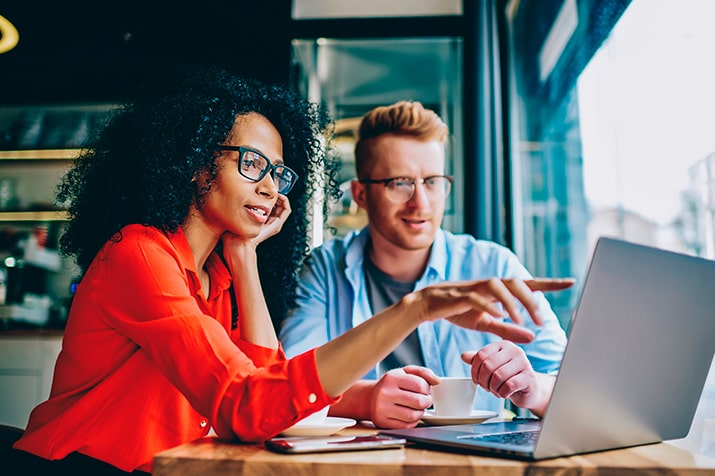O-sistema-de-chamados-SULTS-min - Blog SULTS Sistema de chamados - uma mulher negra e um homem branco no escritório olhando para notebook e analisando algo na tela.