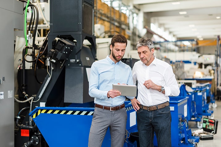 Tipos-de-checklist-manutencao-industrial-SULTS-min - Blog SULTS Tipos de checklist - dois empresários de roupas sociais analisando informação no tablet, de pé, dentro da indústria.