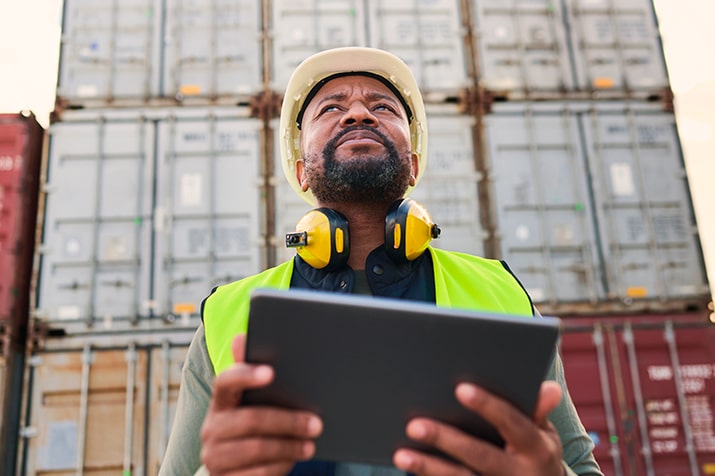 Tipos-de-checklist-transporte-e-logistica-SULTS-min - Blog SULTS Tipos de checklist - colaborador negro segurando tablet e olhando para frente, reflexivo.