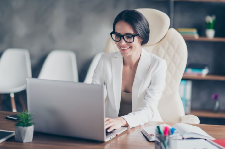 O-SaaS-SULTS-min - Blog SULTS Saas - mulher de negócios em escritório, teclando no laptop e sorrindo.