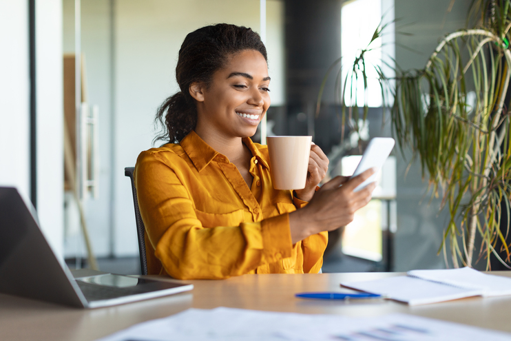 Cheerful african american female manager chatting on cellphone sitting with cup of coffee in office interior - Blog SULTS
